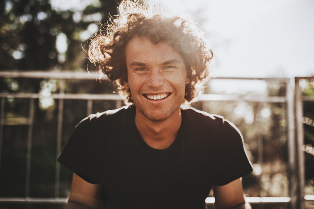 smiling man with curly hair and sun behind him