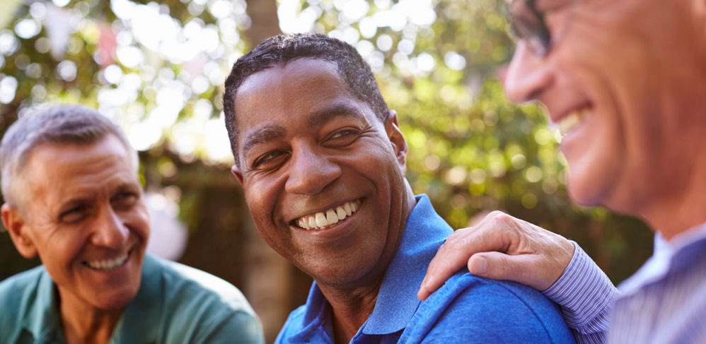 three men smiling with their arms around each other and the beach behind them