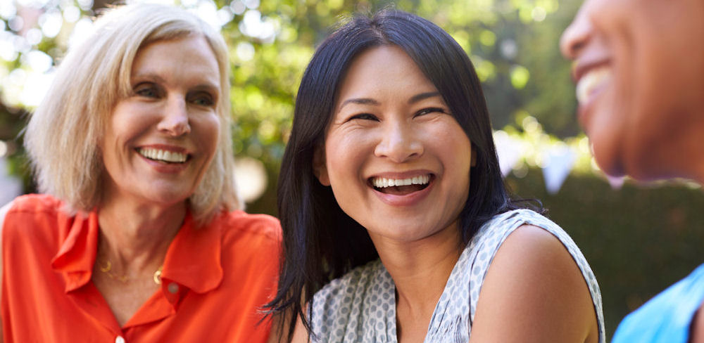 three women outdoors smiling at one another