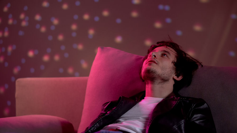 Young man under the influence of party drugs, lost in thought under colorful lights